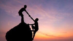 Two people climbing a rock with one helping another up.
