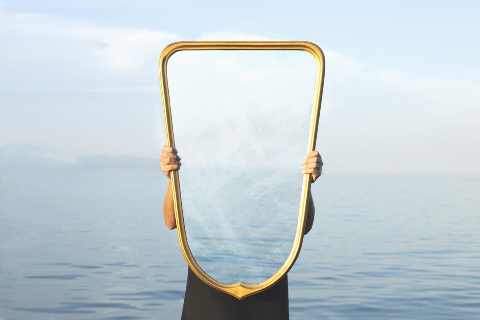 Person holding mirror reflecting the sea view.