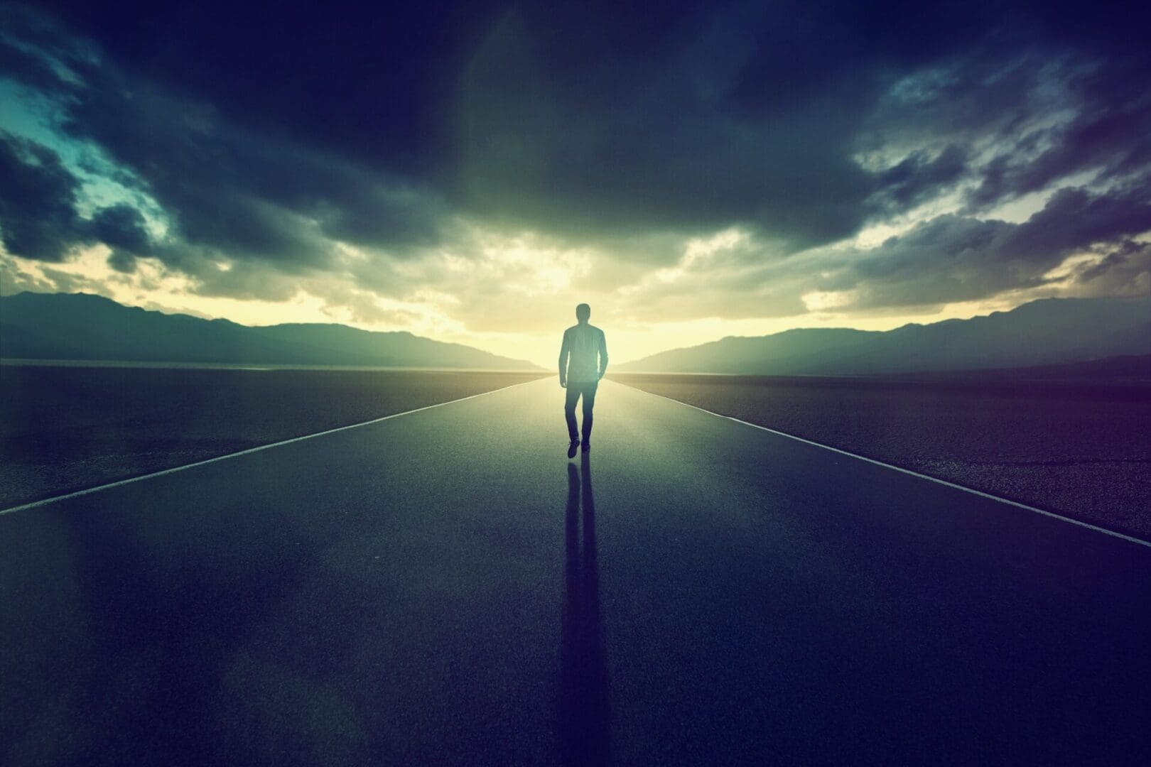 Person walking on road towards bright horizon.