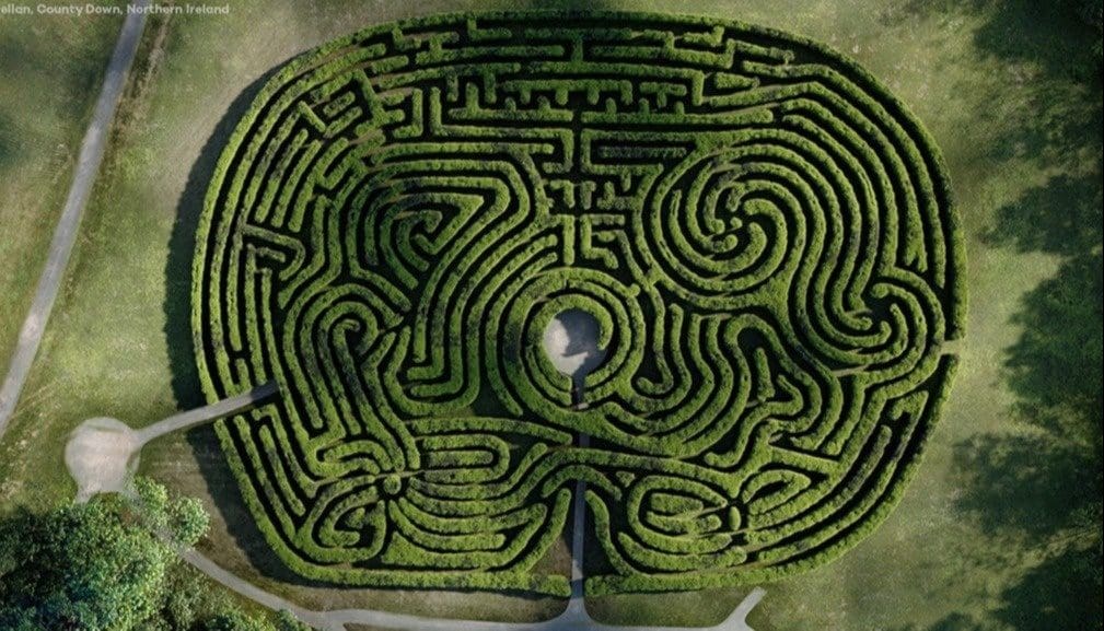Intricate hedge maze from above, sunny day.